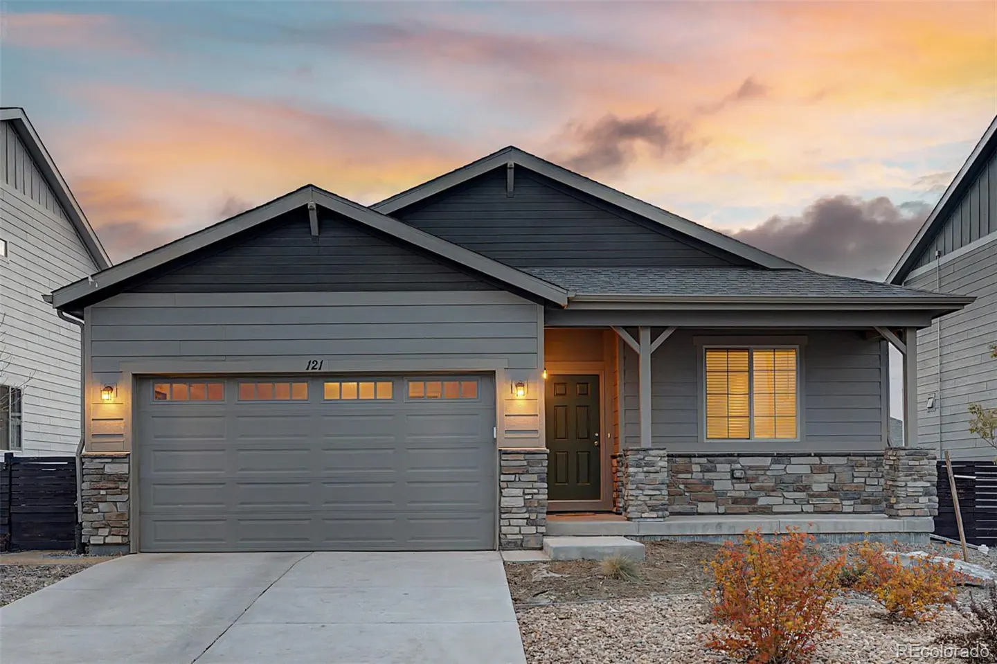 A gray, single-story house with a two-car garage at dusk. The house has stone accents and a dark green front door.