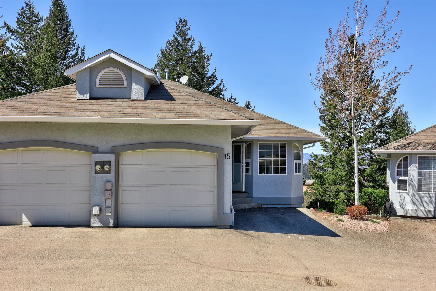 Exterior of a light blue townhouse with two white garage doors, brown roof, and the number 15 on the wall.