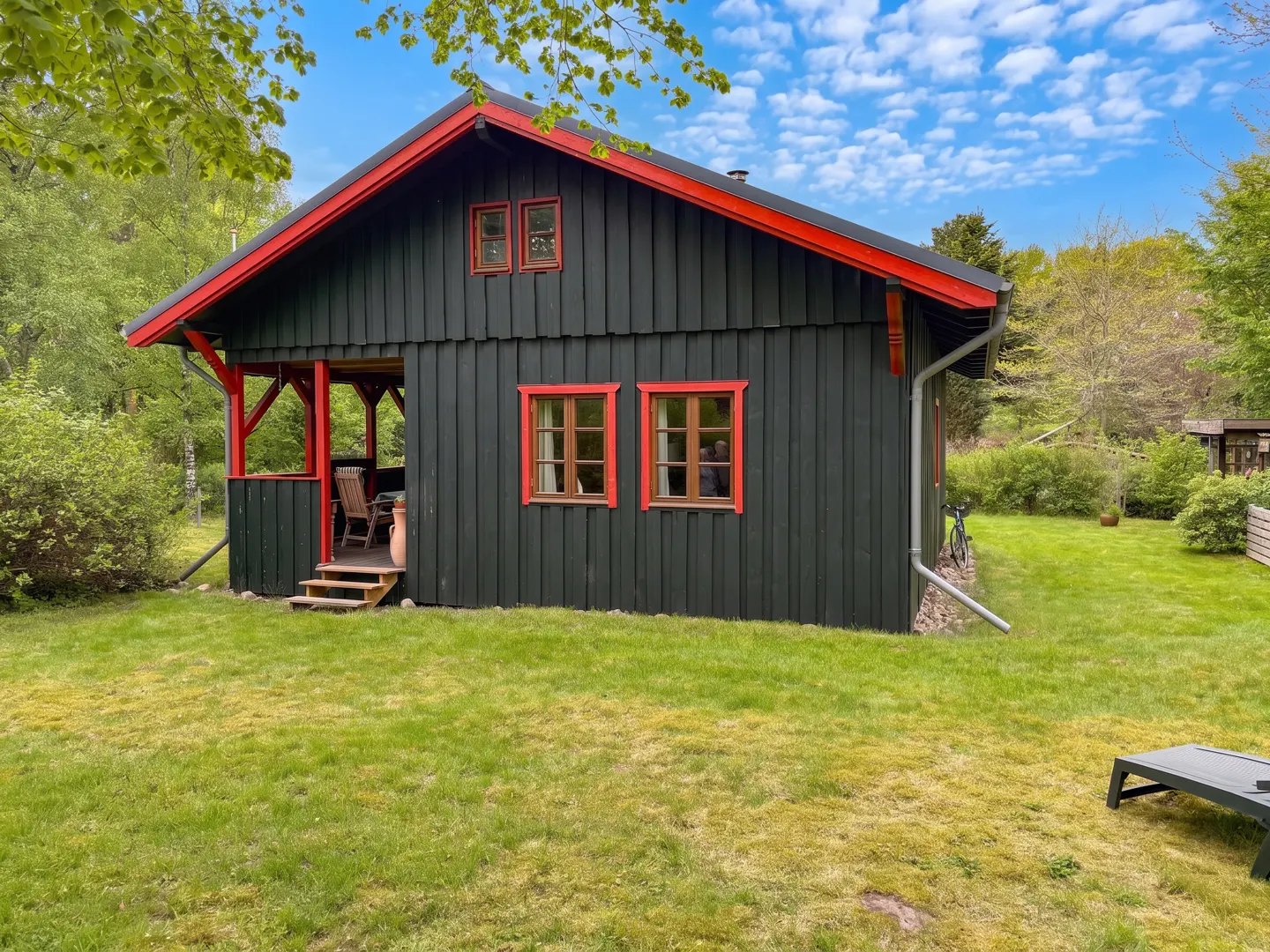 Exterior view of a dark wood cabin with red trim, a porch, and a green lawn.