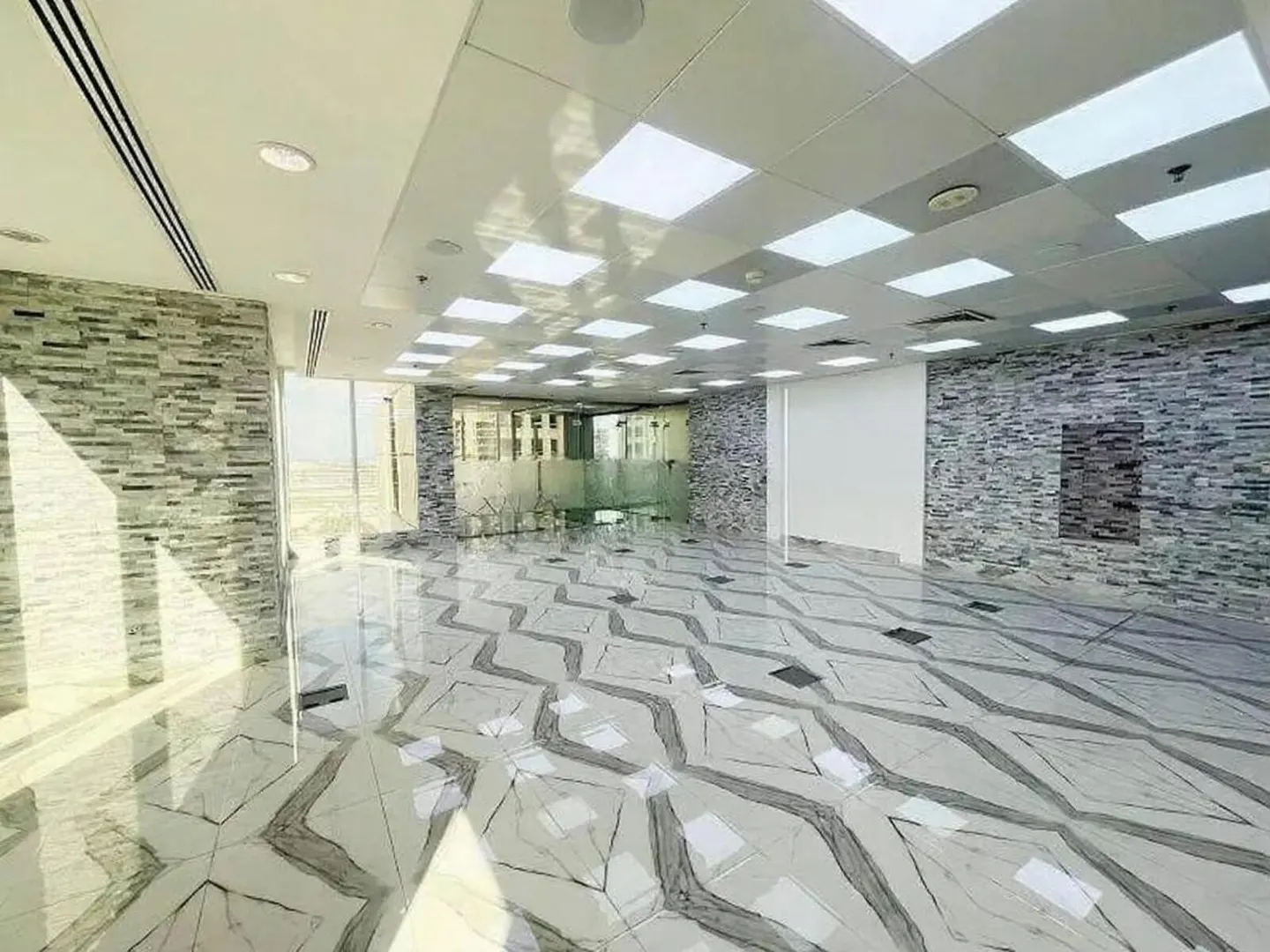Bright, empty office space with white and gray patterned tile floor, stone accent walls, and a glass-walled conference room.