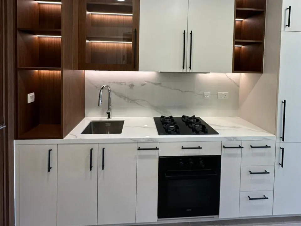 Modern kitchen with white cabinets, black hardware, marble countertops, stainless steel sink, and a black gas cooktop.