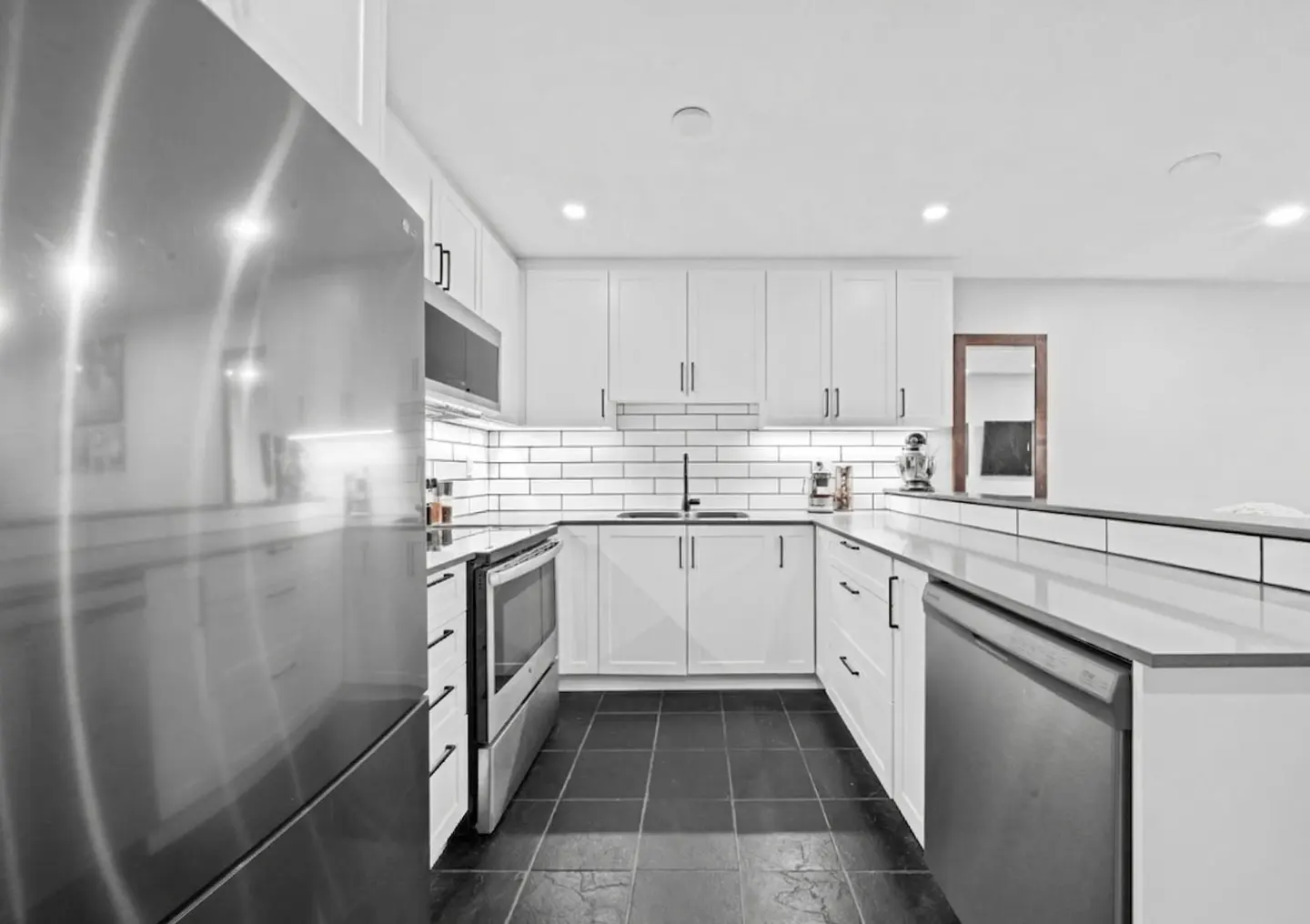 A modern kitchen with white cabinets, black countertops, and stainless steel appliances.