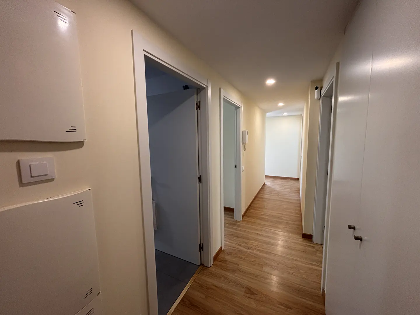 Hallway with light yellow walls, wood floors, and white doors. Heaters are mounted on the left wall.