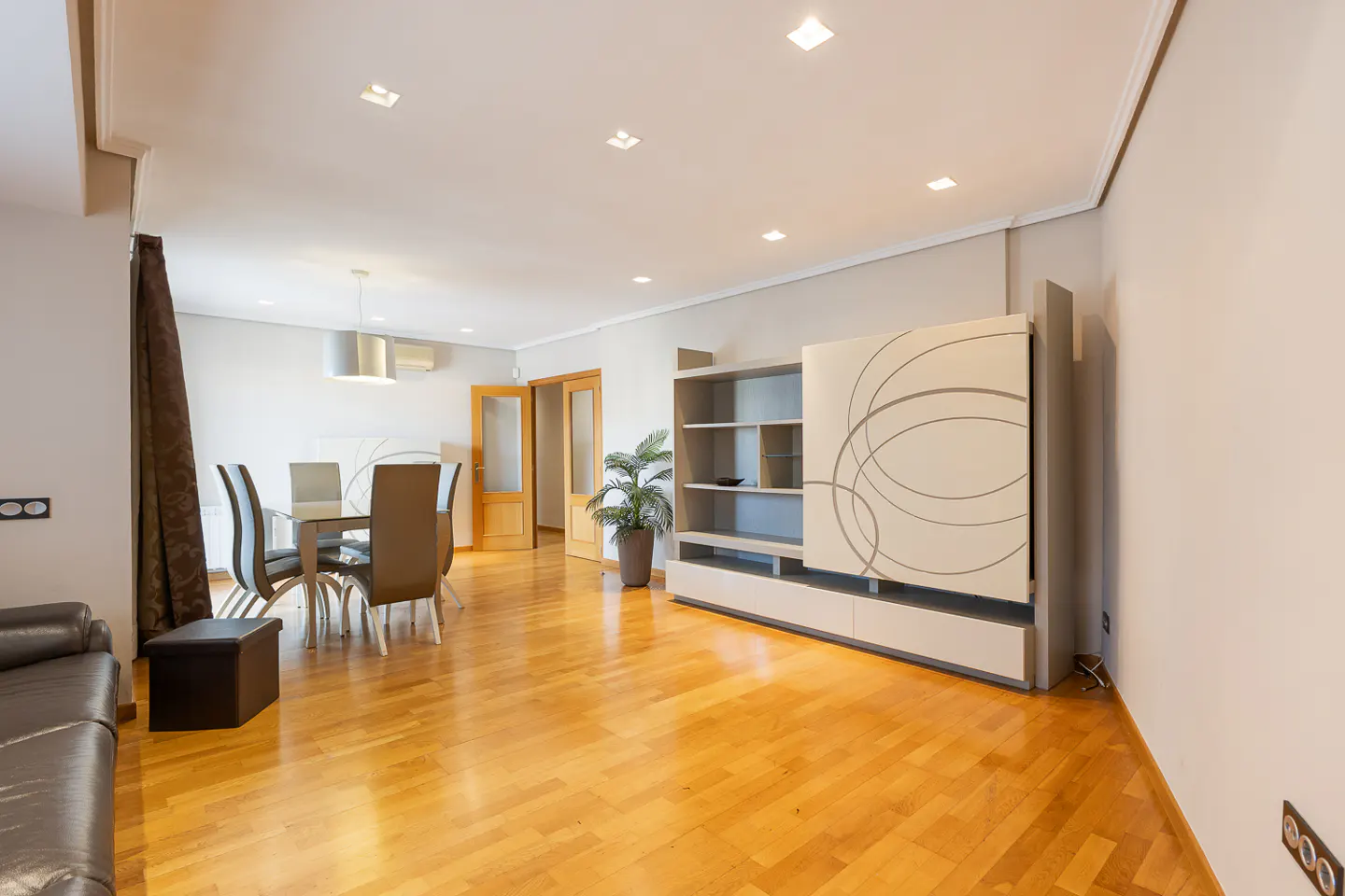 Bright living room with hardwood floors, dining table, brown leather sofa, and a modern entertainment center.