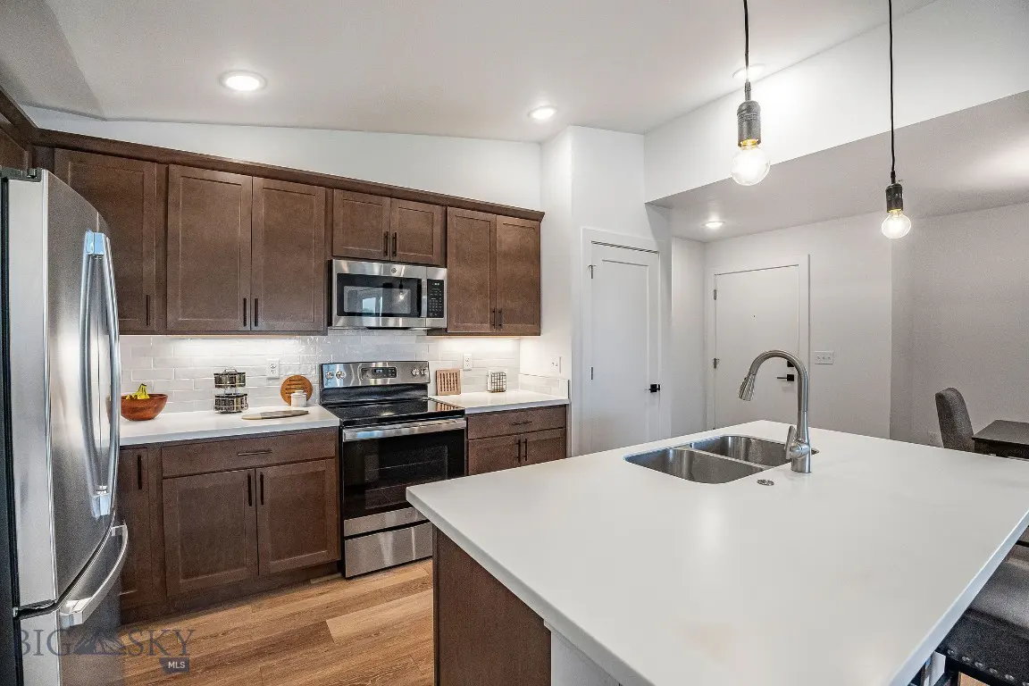 A modern kitchen with brown cabinets, stainless steel appliances, and a white countertop island with a sink.