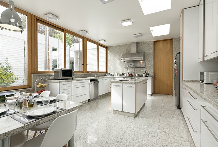 Bright kitchen with white cabinets, granite countertops, and a large window overlooking a courtyard. A table is set for a meal.