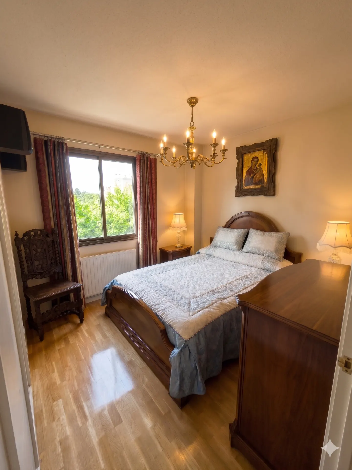 Bedroom with wooden floors, a bed with blue and white bedding, a chandelier, and a window with red curtains.