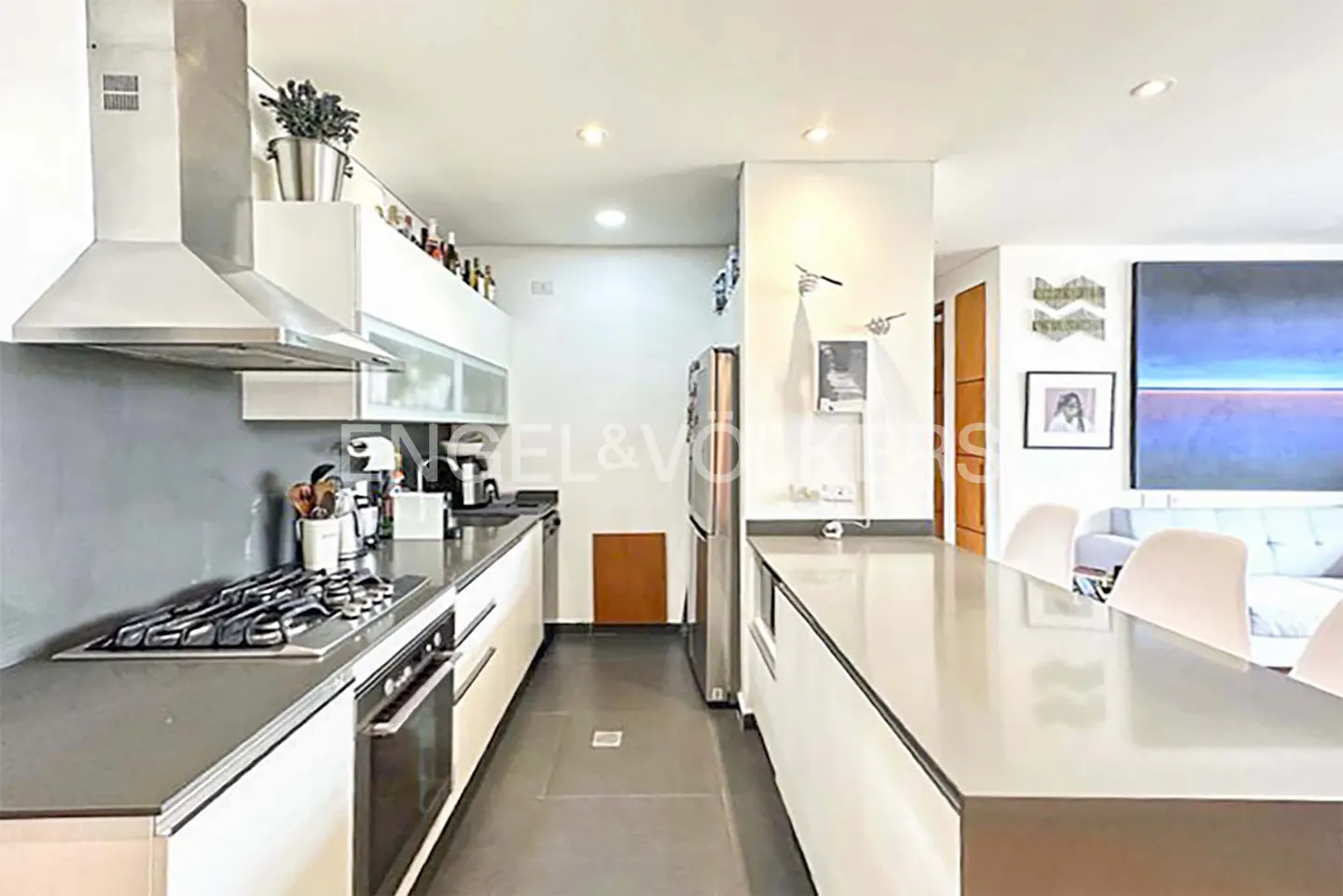 A modern kitchen with white cabinets, gray countertops, stainless steel appliances, and an island with seating.