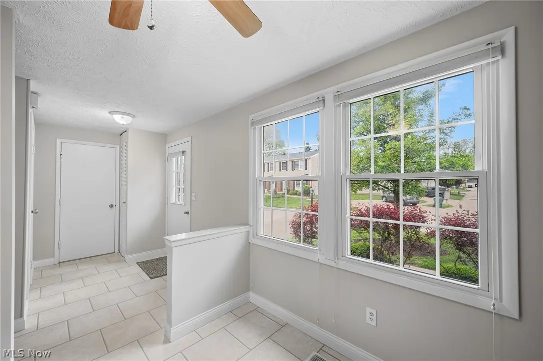 Bright, neutral foyer with tile floor, white walls, and two windows showing a suburban street with trees and houses.