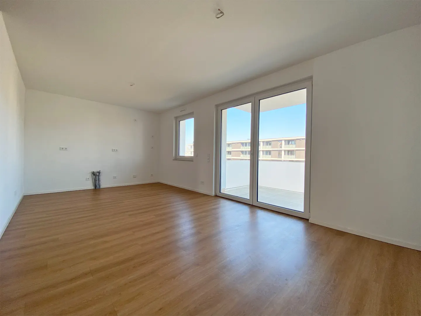Empty room with wood floor, white walls, and sliding glass doors to a balcony. A window is on the left wall.