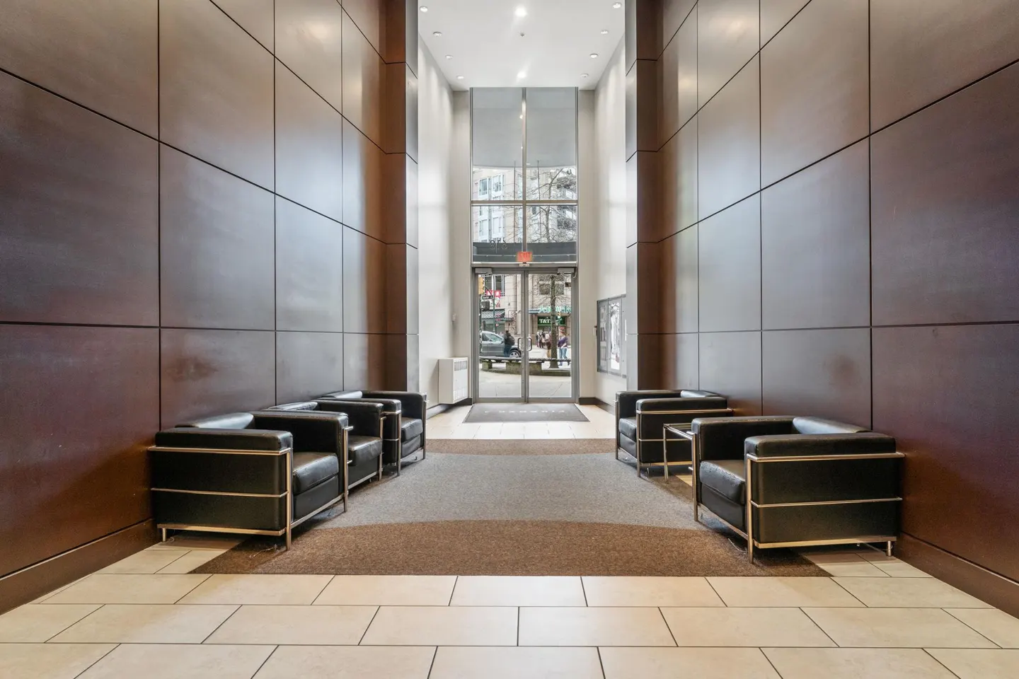 Lobby with black leather chairs, wood paneled walls, and a glass door leading to a city street.