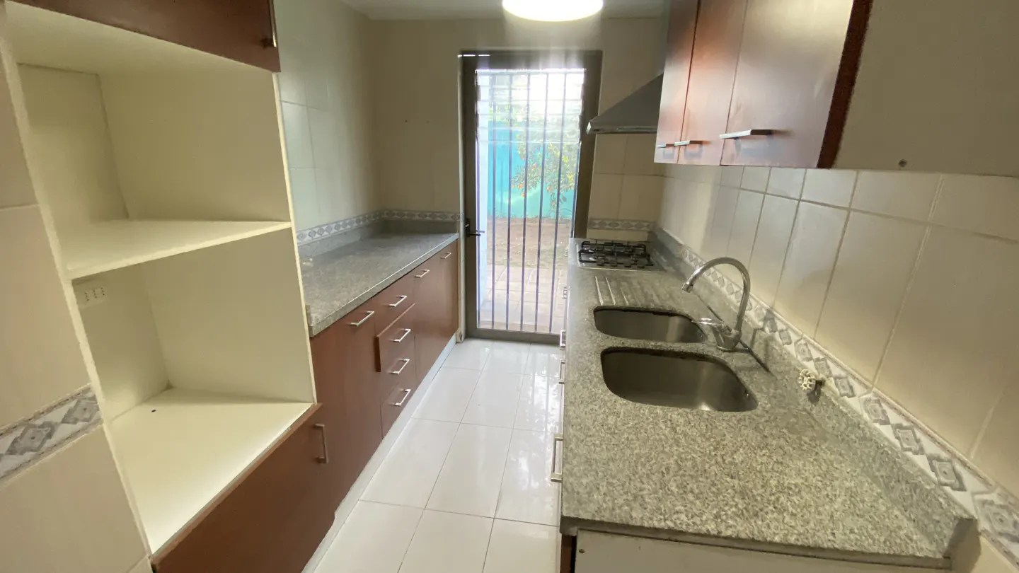 Galley kitchen with brown cabinets, granite countertops, double sink, and a glass door leading to an outdoor area.