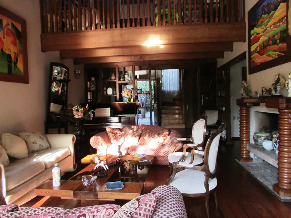 Living room with wood beams, fireplace, and furniture. A painting hangs on the wall. Stairs lead to a second floor.