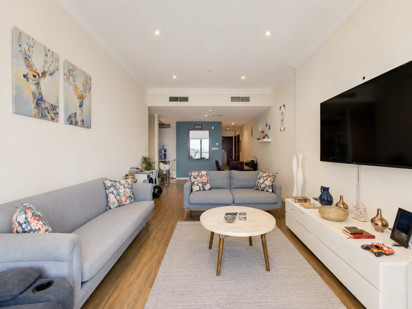 Living room with two gray sofas, floral pillows, a round coffee table, and a white media console with decor. Deer art hangs on the wall.