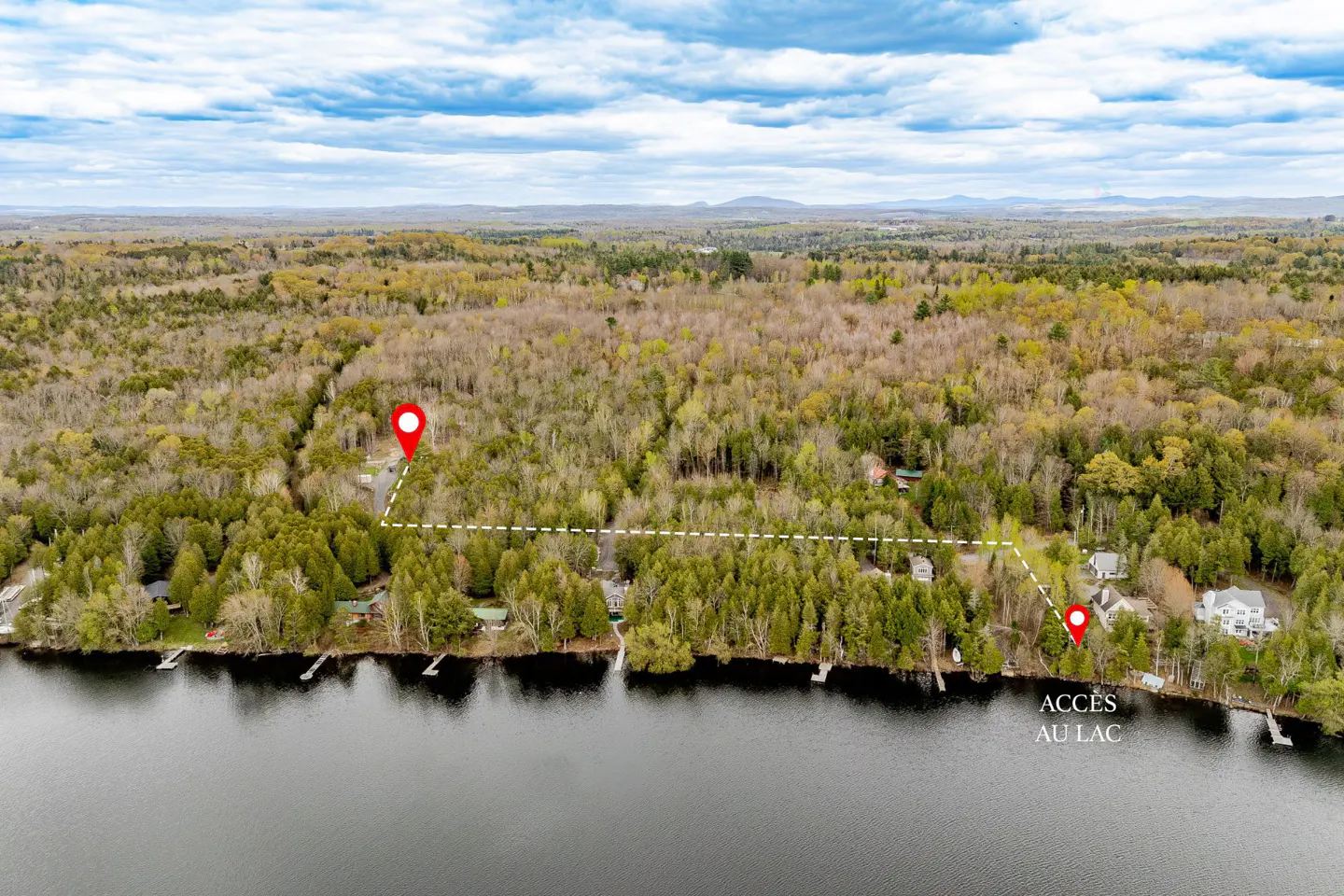 Aerial view of a wooded property with lake access, marked by red pins and a dotted line. "Accès au lac" text is visible.