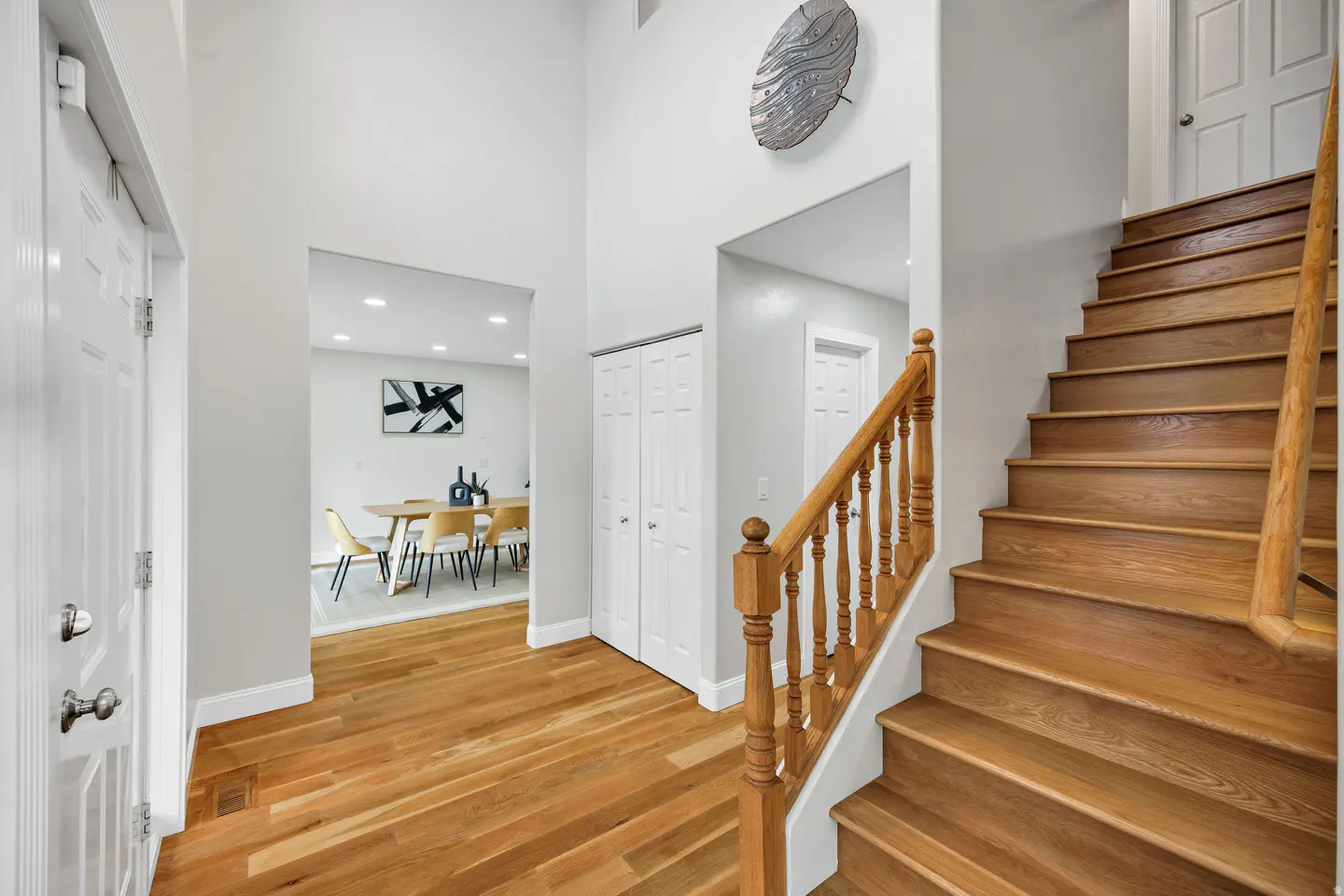 Foyer with hardwood floors, white walls, and a staircase with a wooden banister. A dining room is visible through an archway.