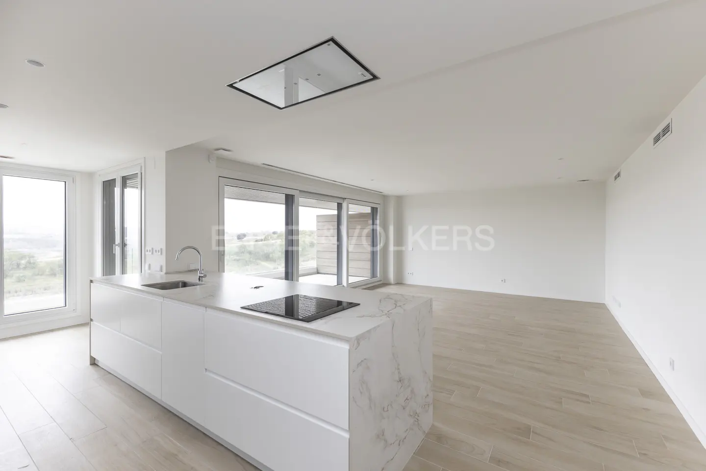 Bright, modern kitchen with white cabinets, marble countertop island, and light wood floors. Large windows offer outdoor views.