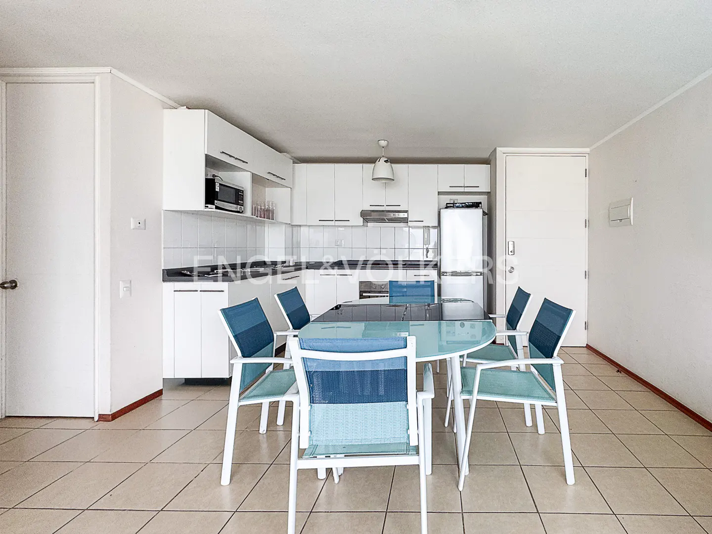 A bright, open kitchen and dining area with white cabinets, a glass table, and blue chairs.