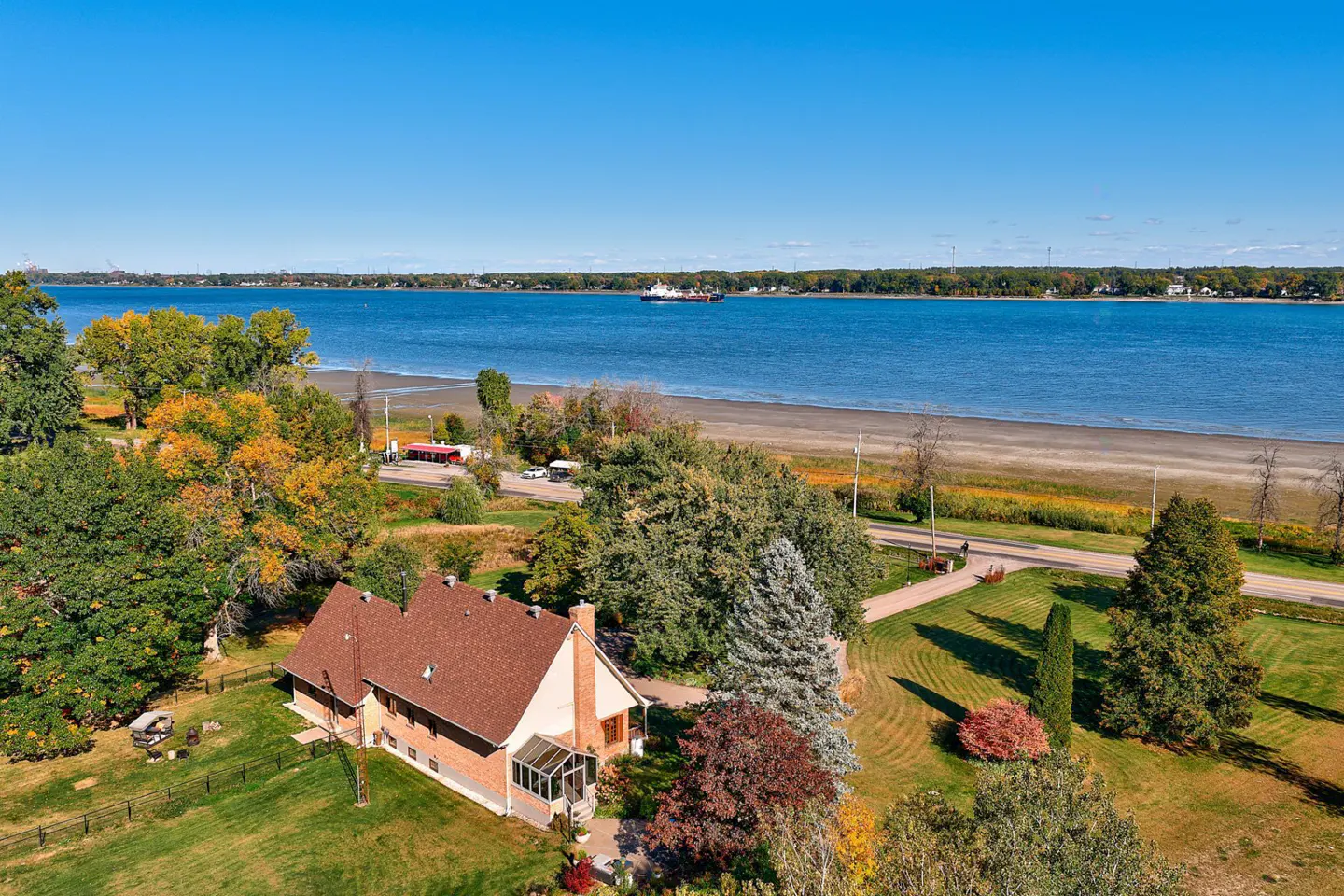 Aerial view of a brick house with a brown roof, green lawn, and a blue lake in the background.