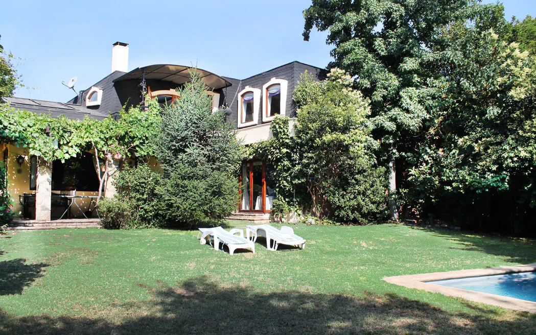 Exterior view of a house with a black roof, green lawn, pool, and two white lounge chairs.