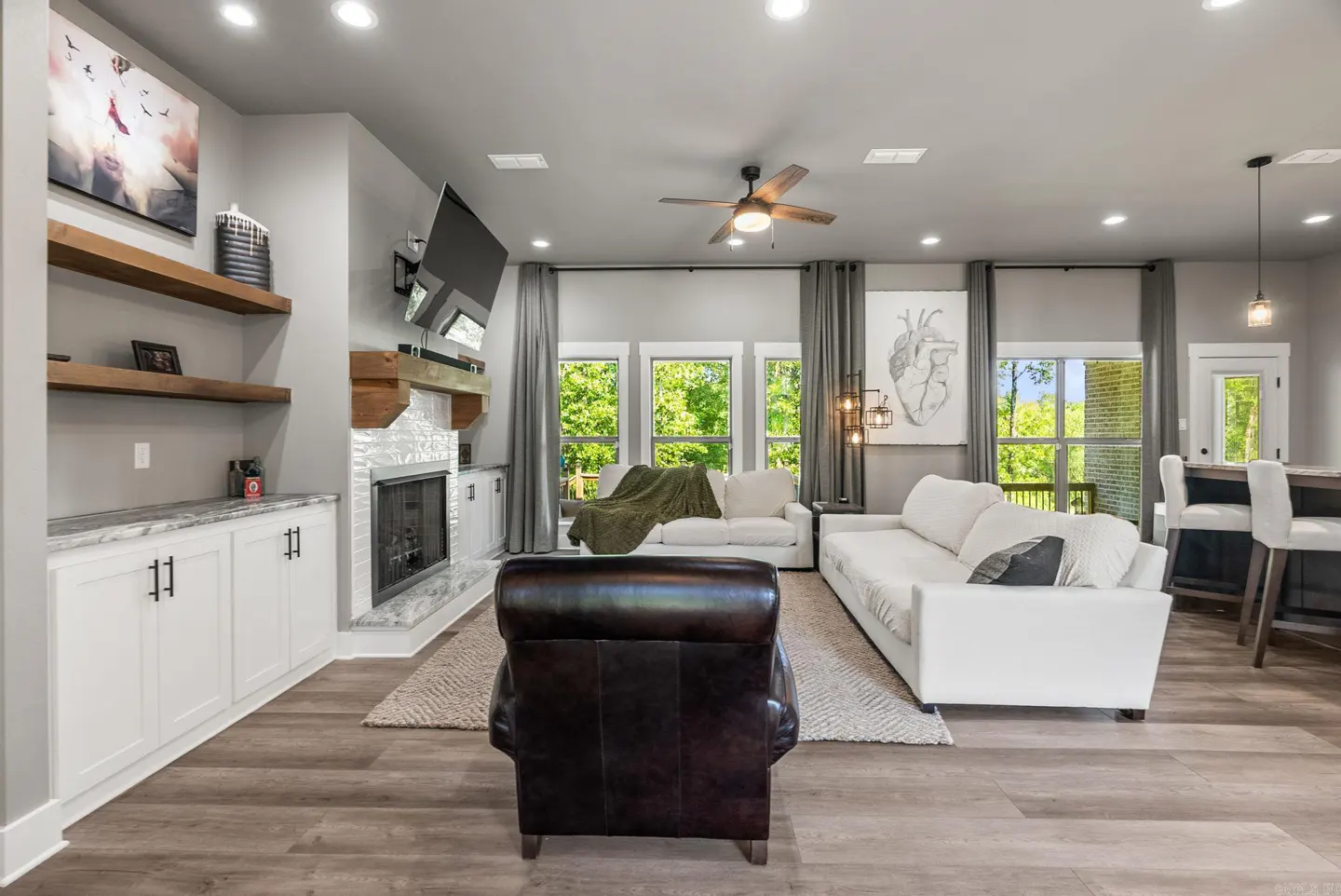 Living room with white sofas, a fireplace, and a dark leather chair on a wood floor.