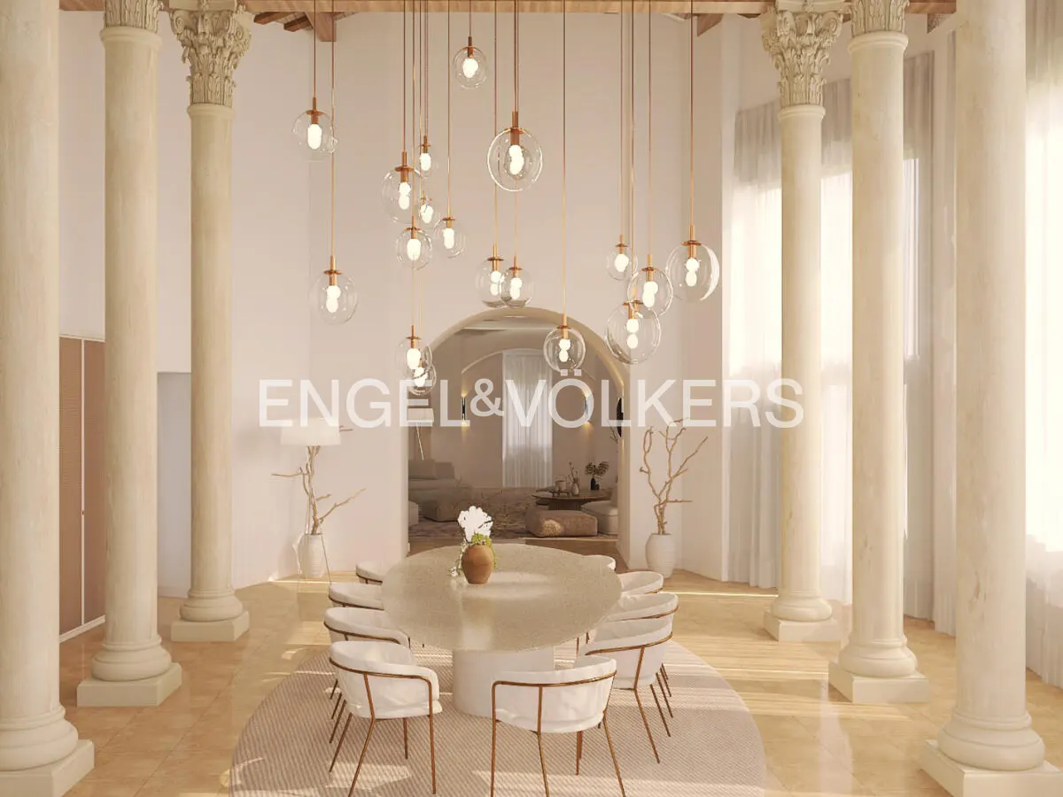 Elegant dining room with white columns, a round table with white chairs, and hanging glass pendant lights. Engel & Volkers logo visible.
