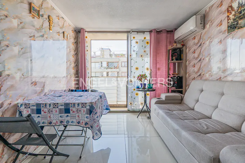 Living room with marble-patterned walls, a gray sofa, a table with a blue patterned tablecloth, and a balcony with pink curtains.