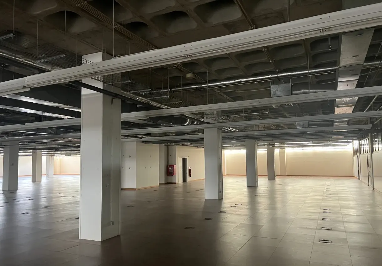A large, empty commercial space with concrete floors, white support columns, and exposed ceiling fixtures.