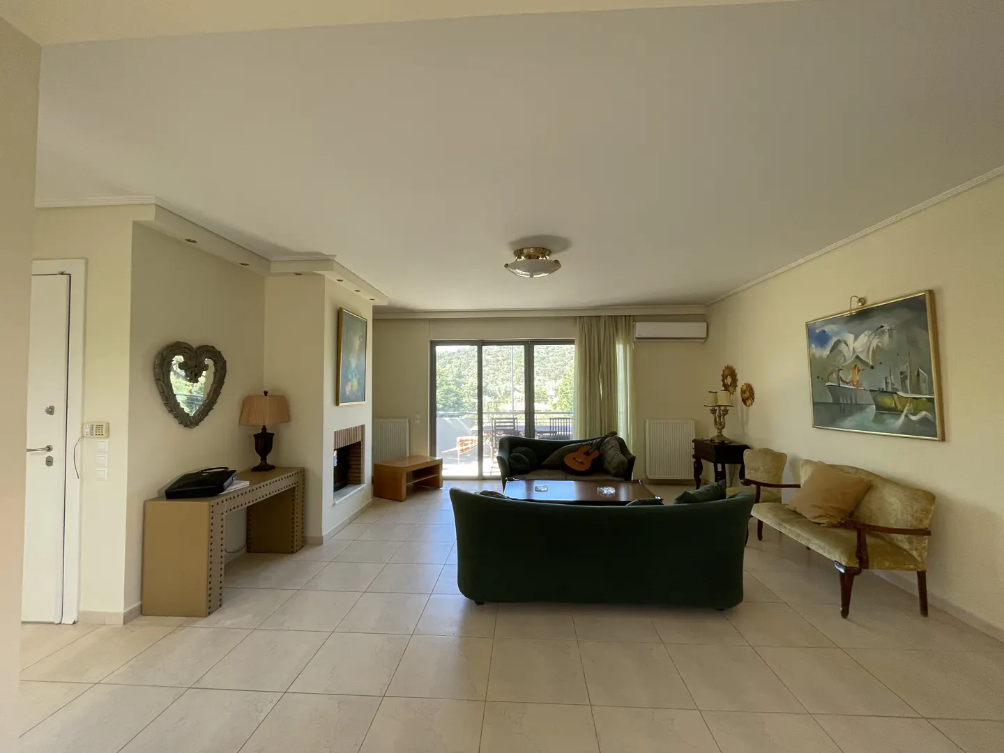 A spacious living room with green sofas, a fireplace, and a balcony with a view.