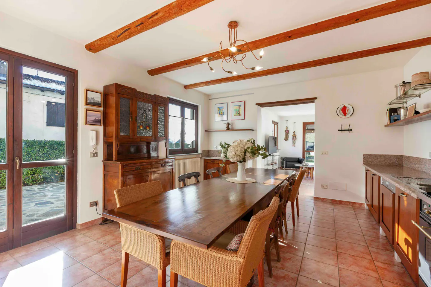 A dining room with a long wooden table, wicker chairs, and exposed wooden beams on the ceiling.