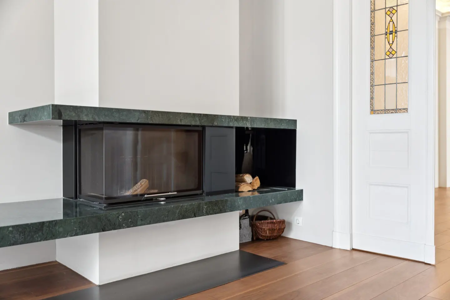 Living room with a green marble fireplace, wood logs, and a white door with stained glass.