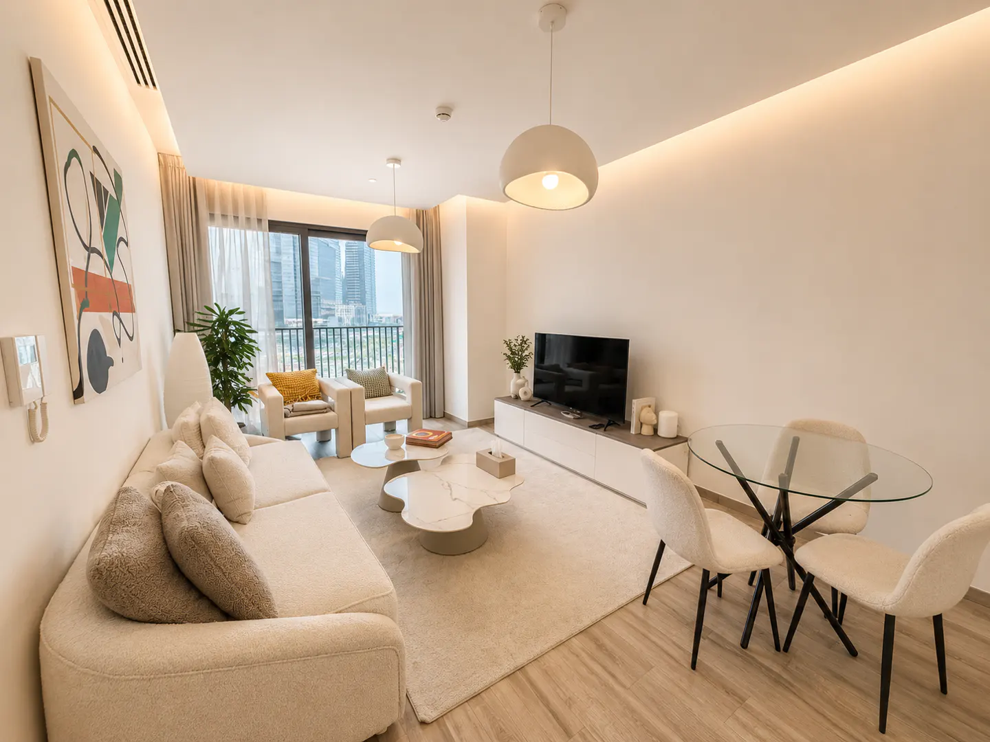 Bright, modern living room with a white sofa, chairs, and a glass table. A large window shows a city view.