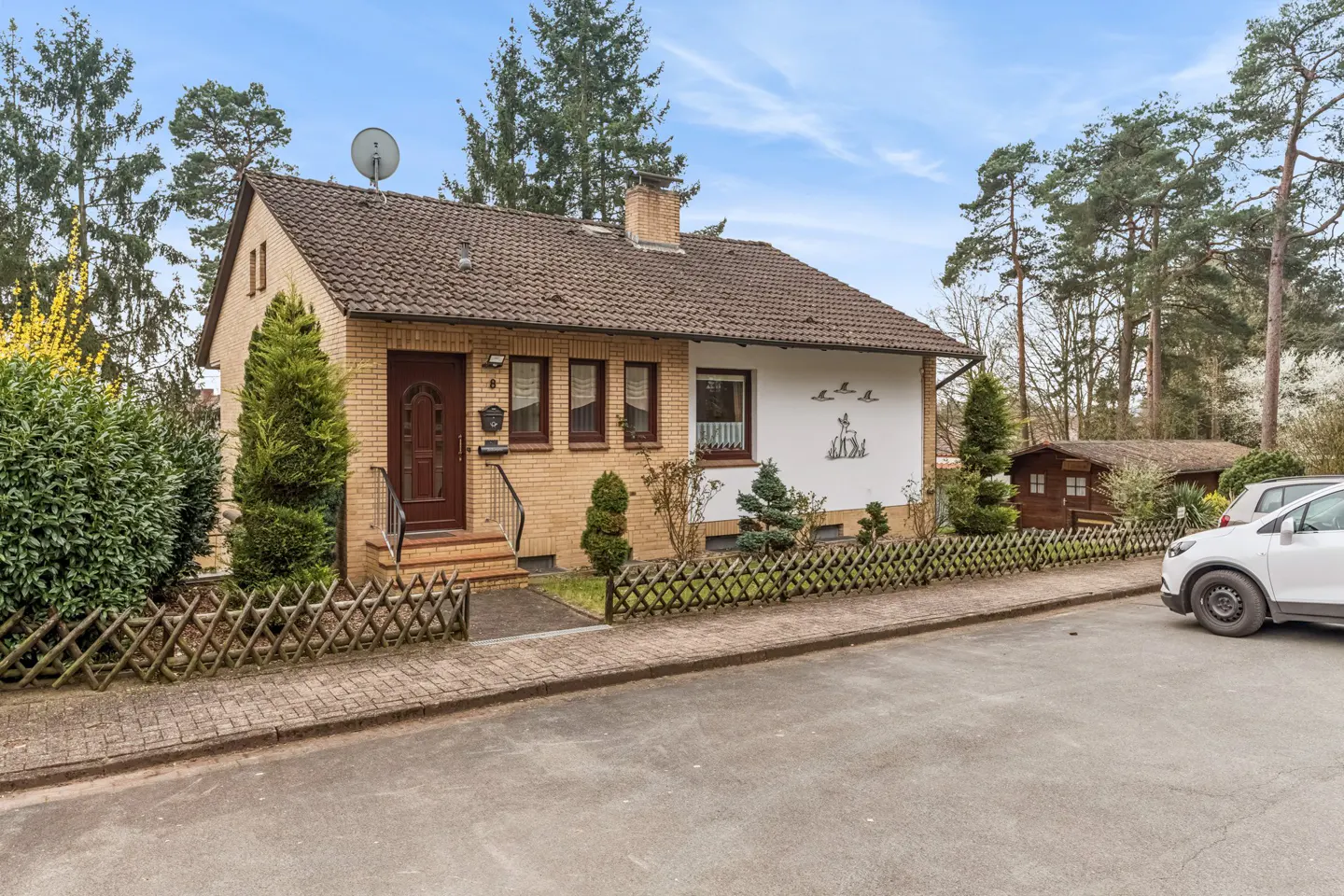A one-story brick house with a brown roof, a satellite dish, and a small yard.