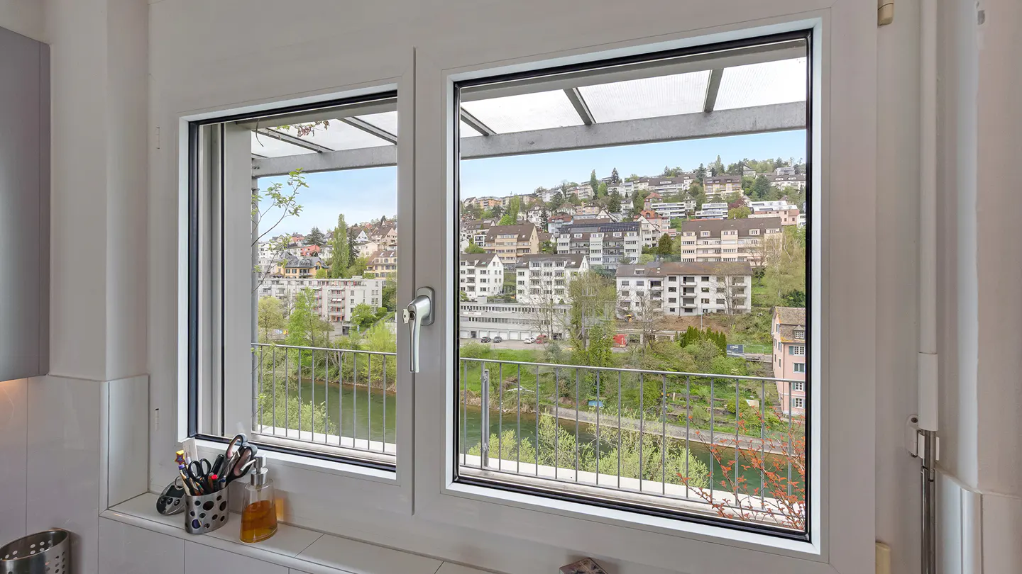 A white-framed window offers a view of a hillside town, a river, and a balcony.