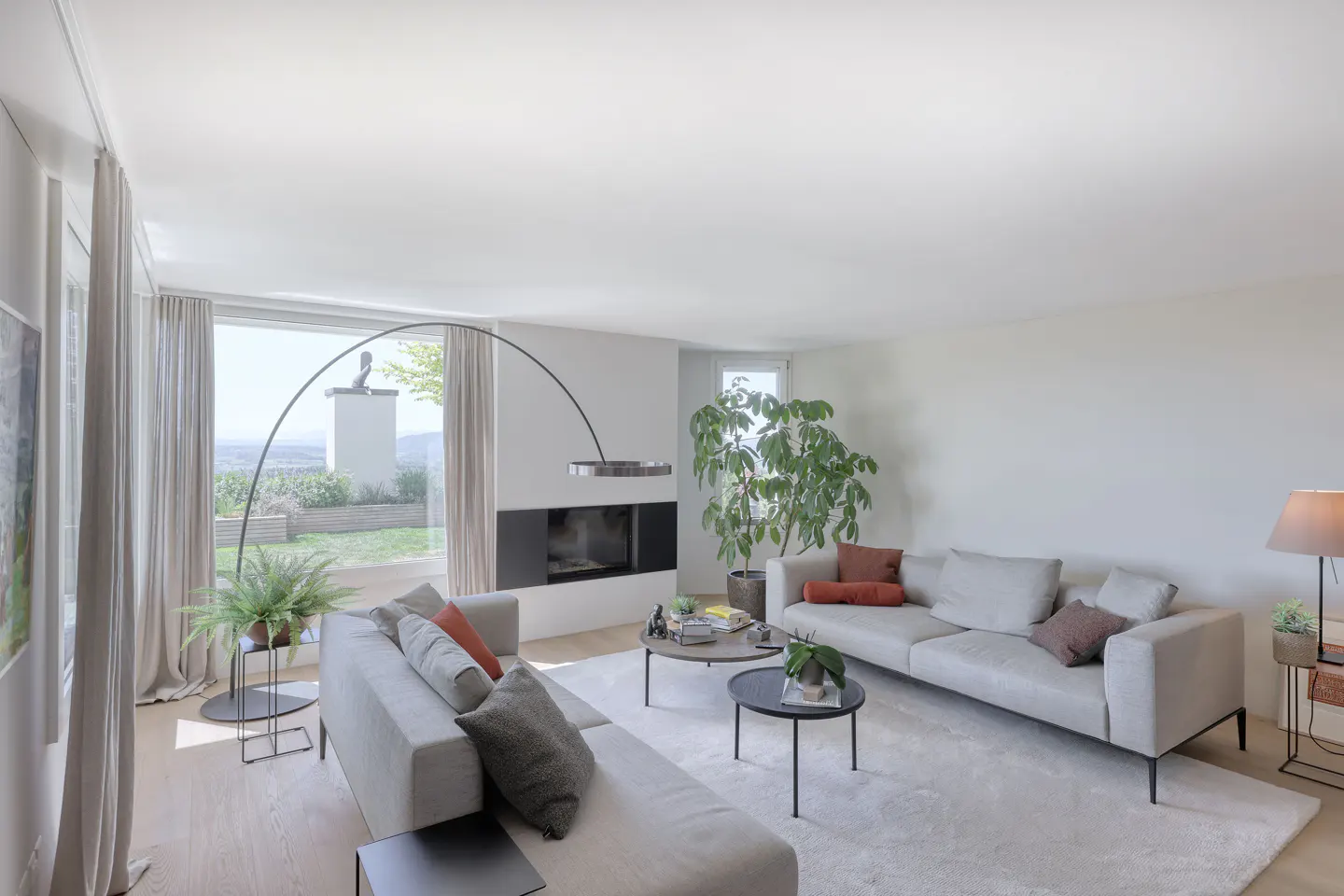 Bright living room with two gray sofas, a fireplace, and large windows overlooking a green landscape.