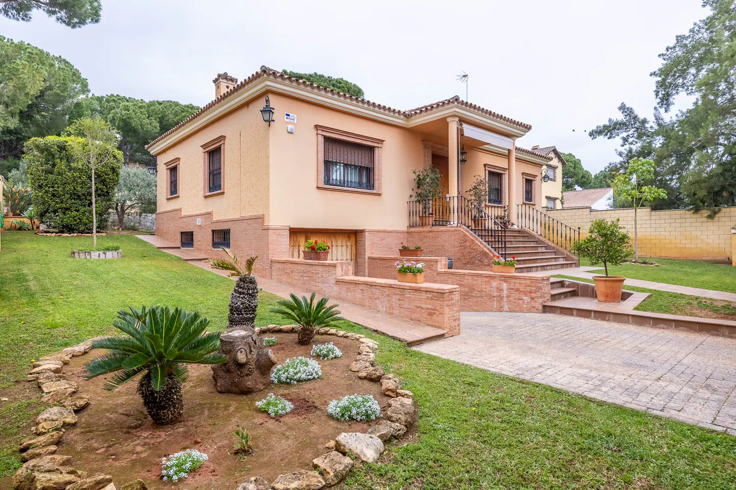 Exterior view of a peach-colored, two-story house with a red tile roof, a brick foundation, and a well-manicured lawn.