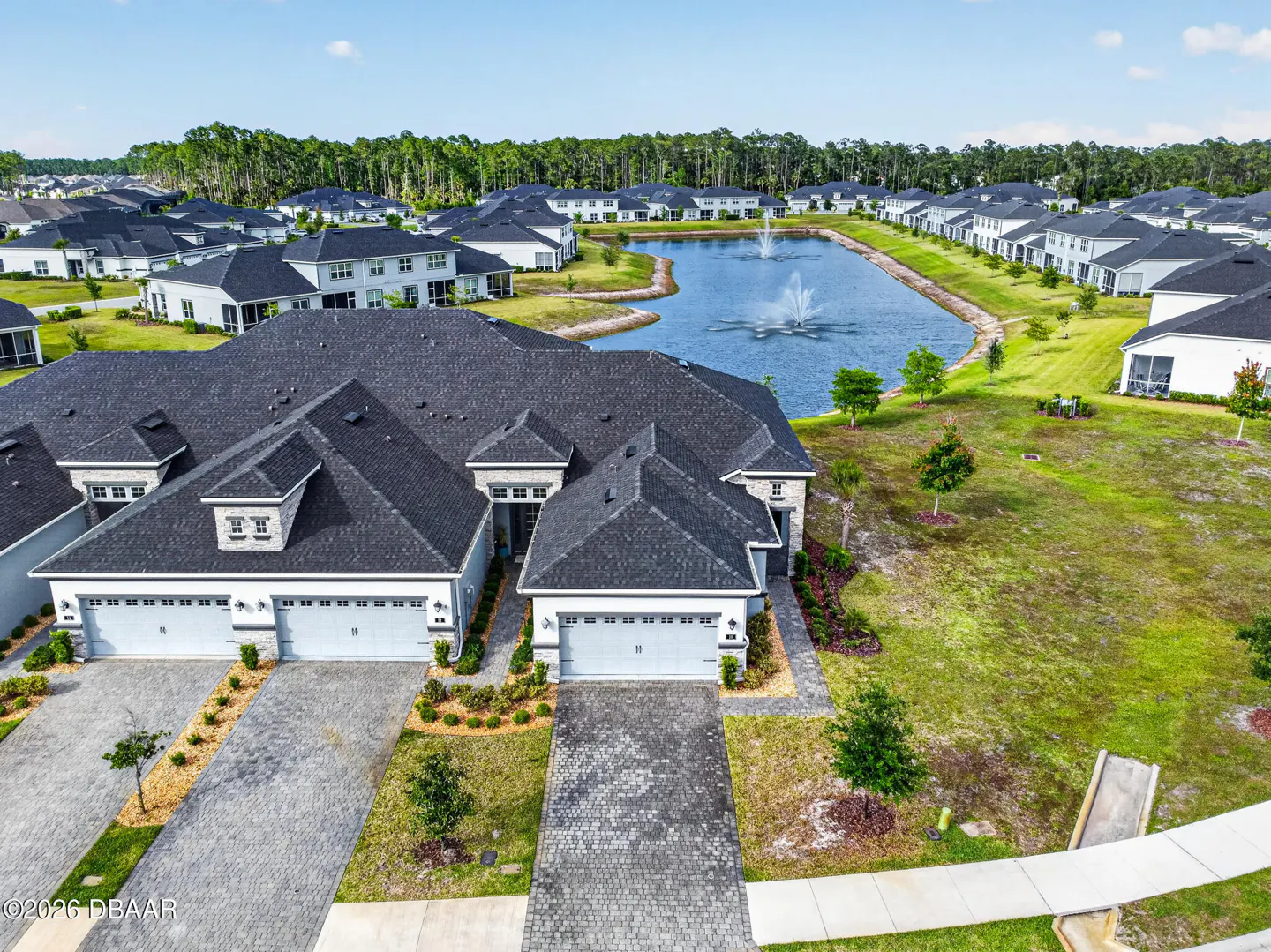 Aerial view of a light blue, modern townhouse with a dark gray roof, in a community with a pond and fountain.