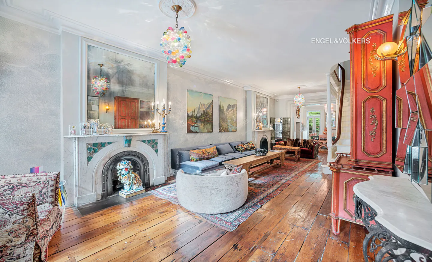Elegant living room with hardwood floors, a marble fireplace, colorful glass chandelier, and ornate red antique cabinet.