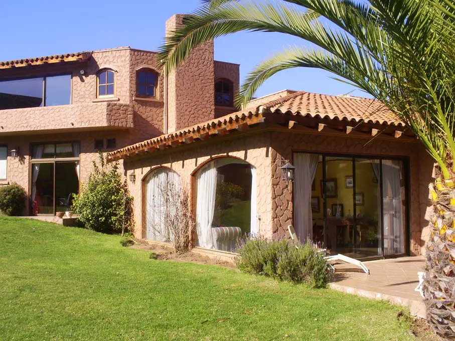 Exterior view of a two-story house with a stone facade, terracotta roof, green lawn, and palm tree.