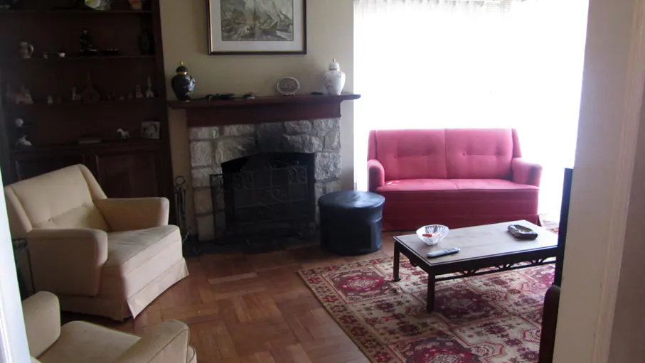 Living room with a stone fireplace, red sofa, beige armchairs, and a patterned rug on a wood floor.