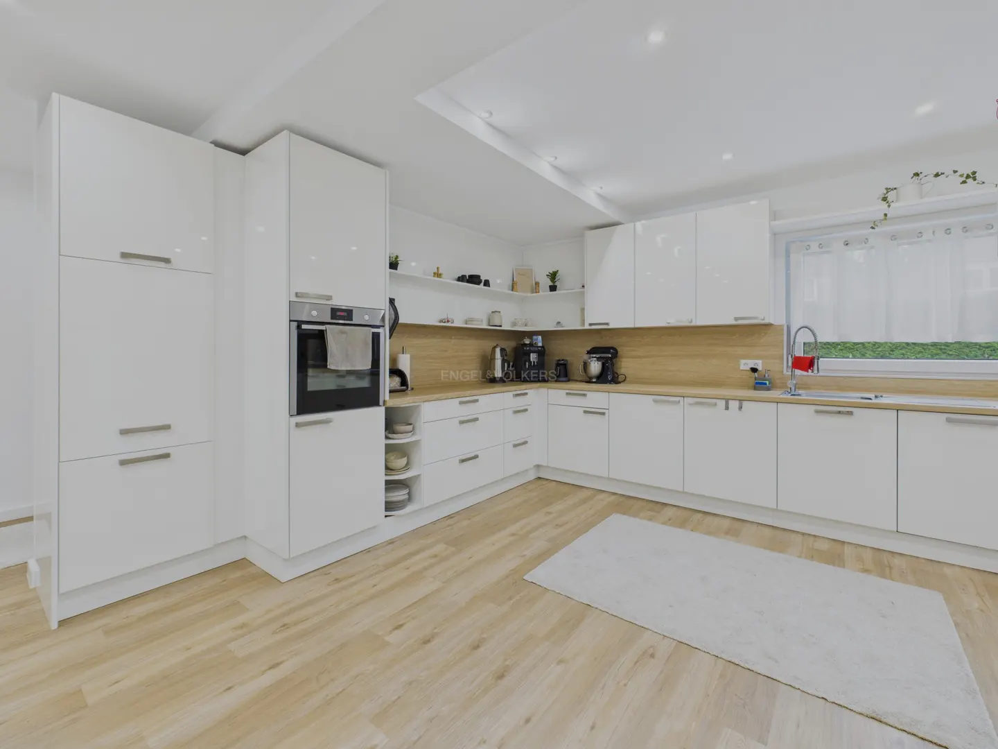 Bright, modern kitchen with white cabinets, wood countertops, and light wood floors. A white rug sits in the center. Appliances are stainless steel.