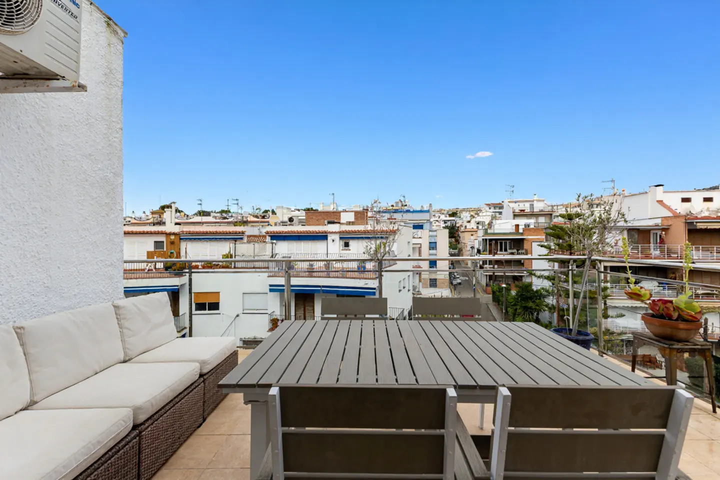 Balcony view with a gray table and chairs, a white sofa, and a cityscape under a blue sky.