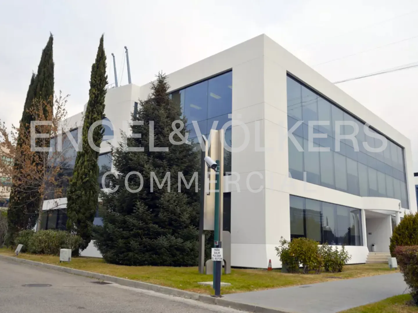 Modern white commercial building with large windows and green landscaping. Engel & Volkers Commerce logo is visible.
