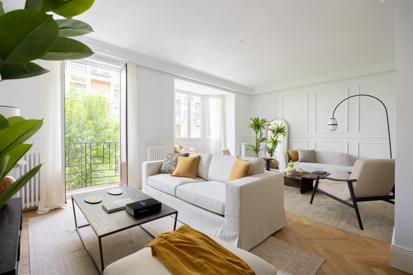 Bright, modern living room with white walls, a white sofa with mustard pillows, a dark coffee table, and a balcony view.