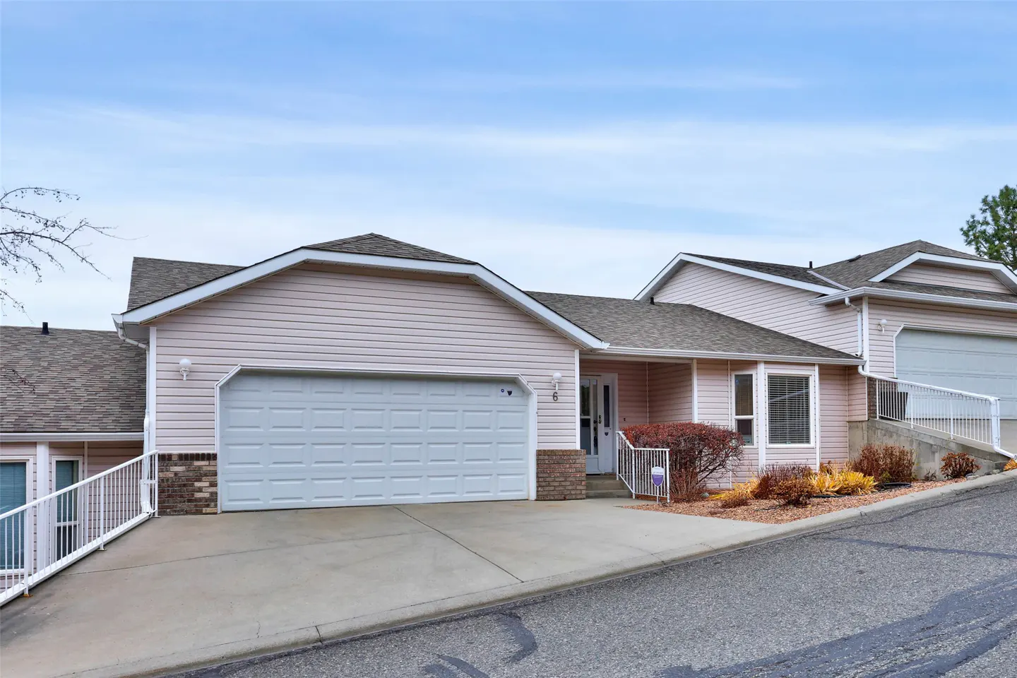 A light pink house with a white garage door and a gray roof on a cloudy day.