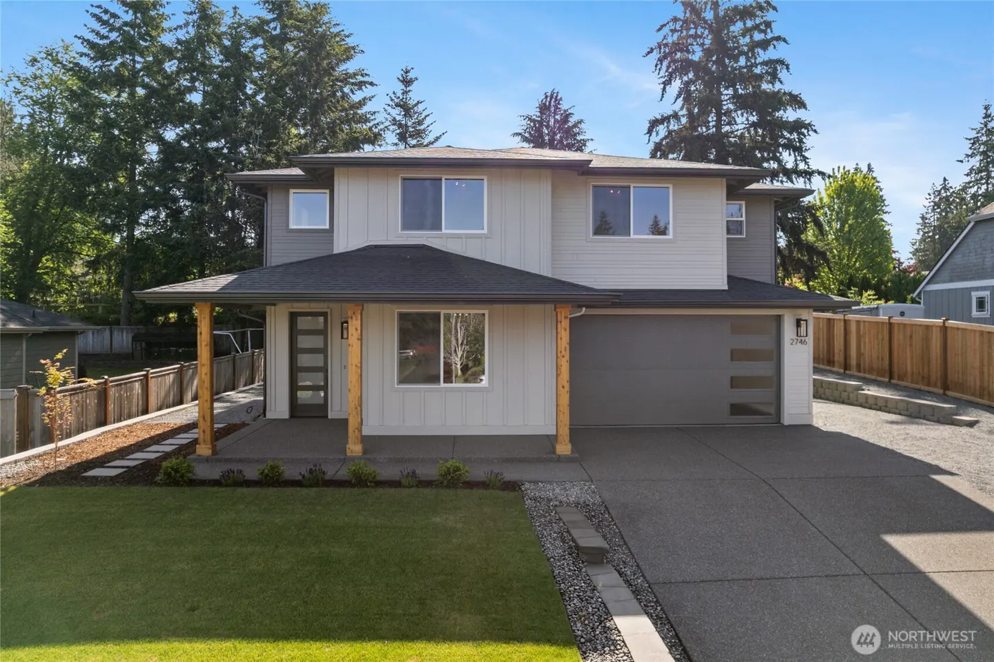 Two-story home with gray siding, a black roof, and a covered porch with wooden pillars. A green lawn and driveway lead to the house.