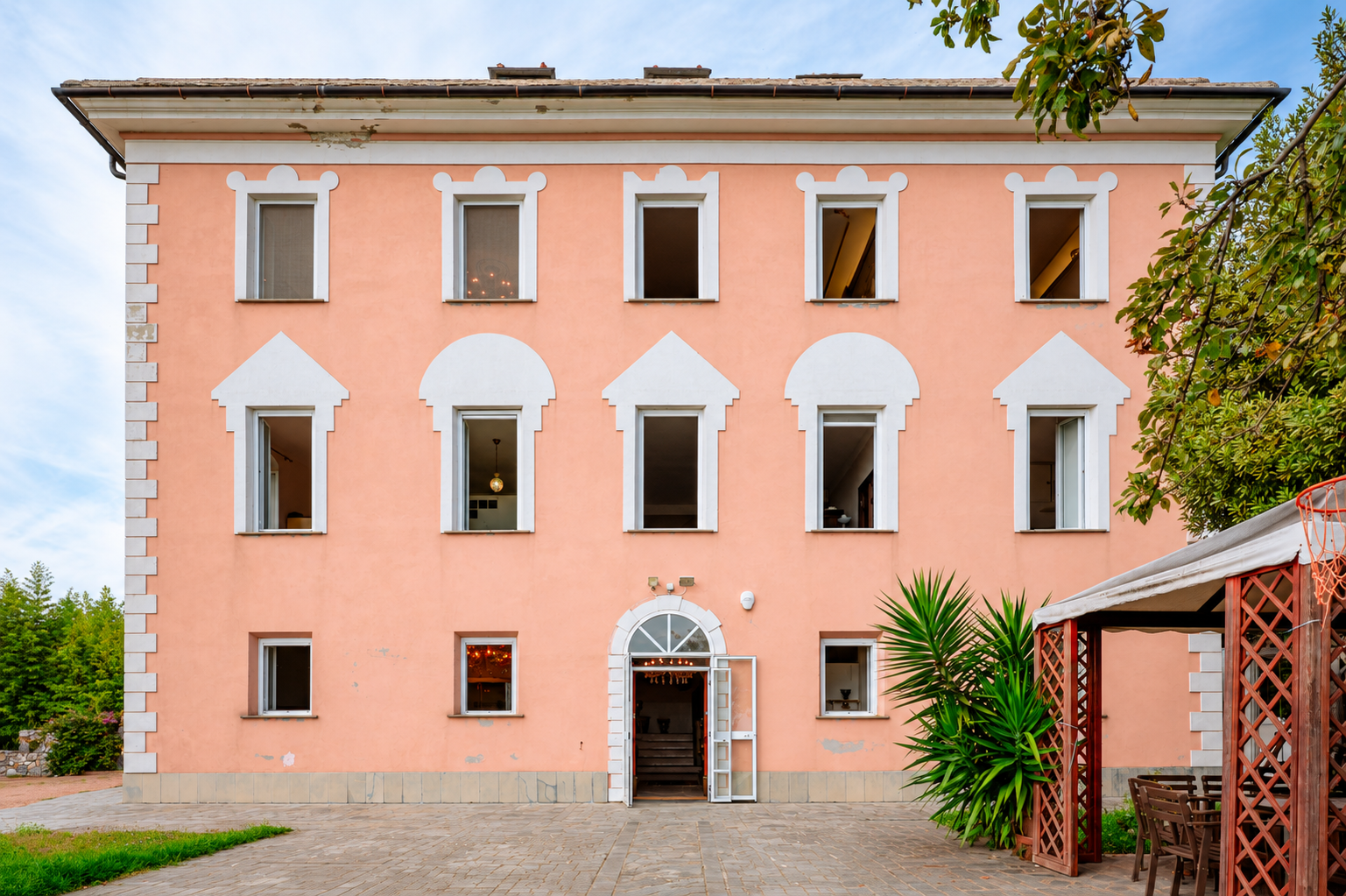 A three-story peach-colored villa with white trim, symmetrical windows, and an arched entrance on a paved patio. [AI-generated text]