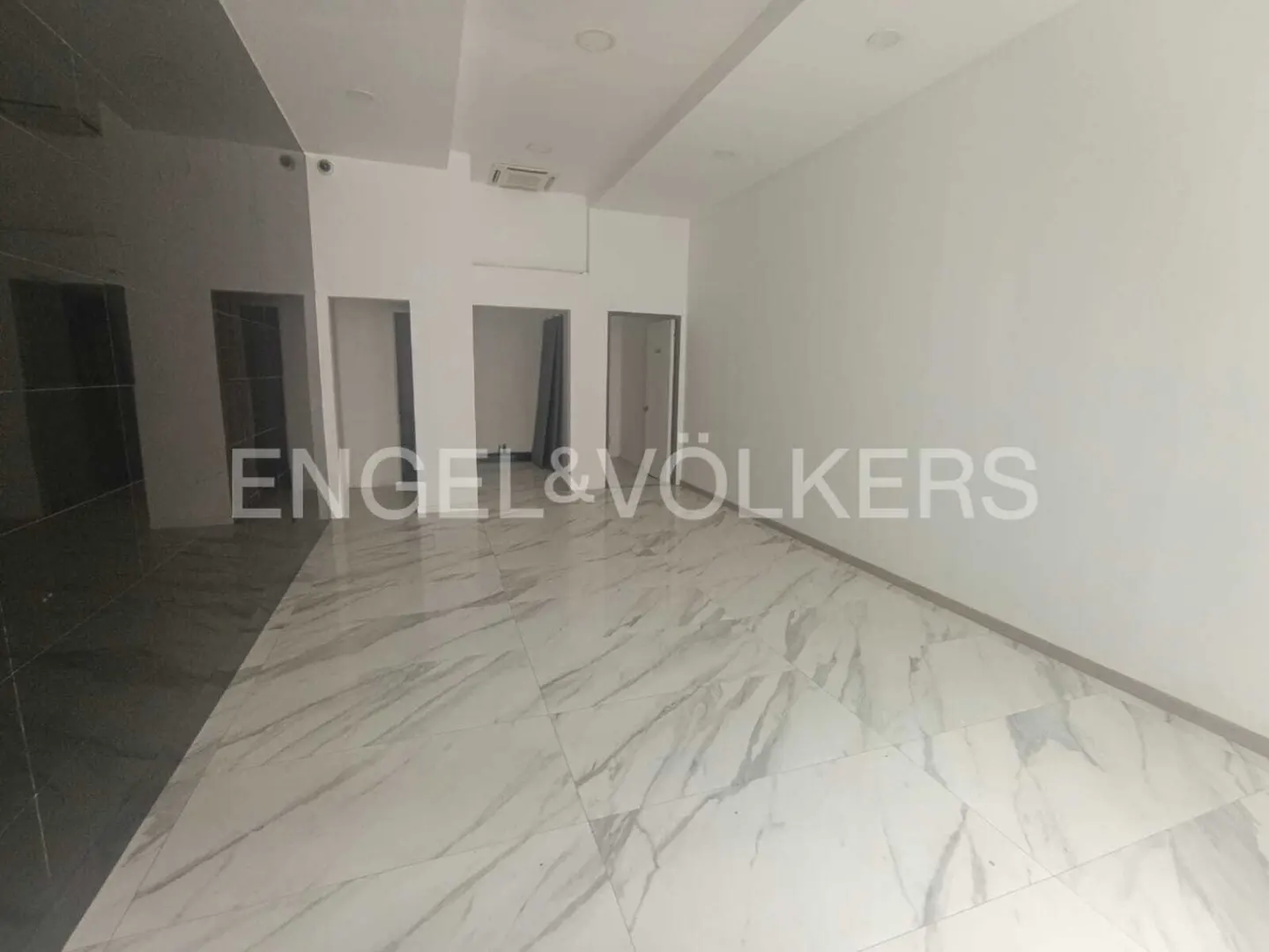 Empty commercial space with white walls, marble floors, and several doorways. Engel & Völkers logo is visible.