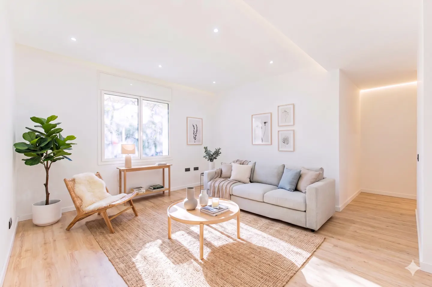 Bright living room with white walls, light wood floors, and a beige sofa. A woven rug sits under a round coffee table. A fiddle-leaf fig tree adds a touch of greenery.