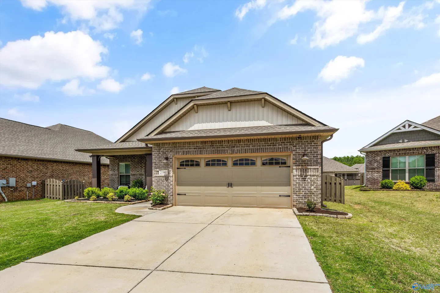A single-story brick house with a beige garage door, green lawn, and blue sky with white clouds.